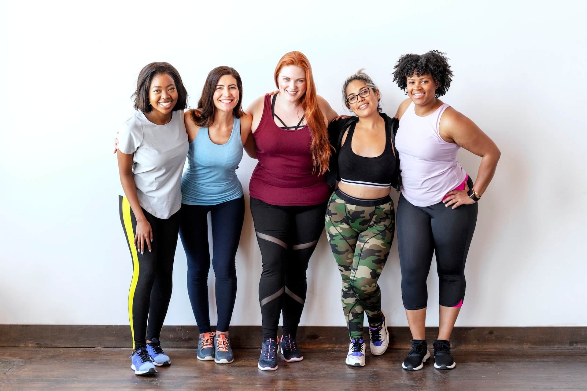 Group of five ladies in gym outfits holding arms and smiling | Featured Image for the virtual gastric band hypnosis service page from HypnoFit.